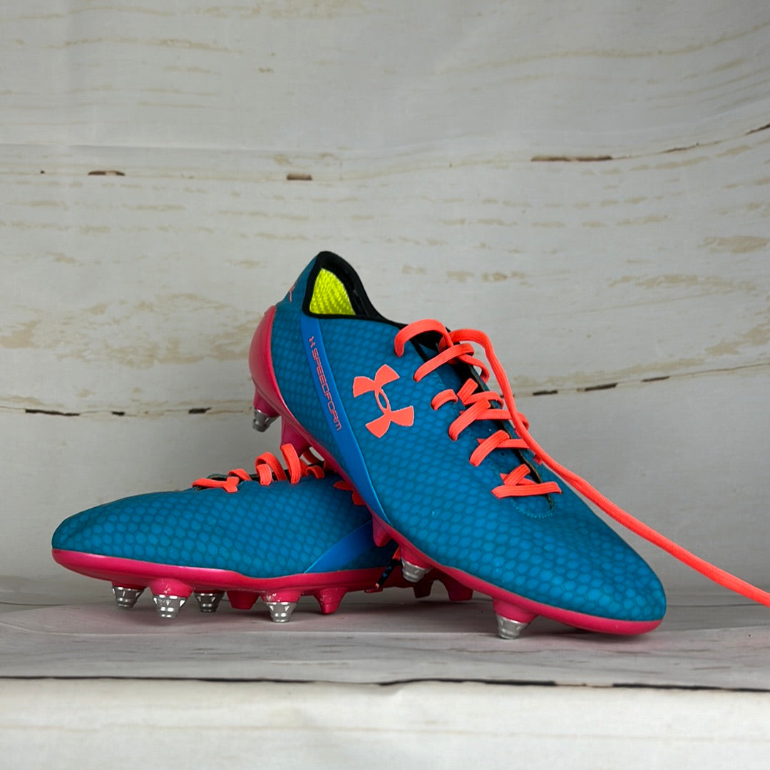 A pair of blue and pink Under Armour football boots with 'Memphis' written on the back, positioned on a wooden surface.