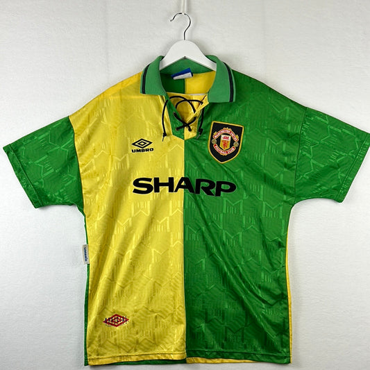 Manchester United green and gold third shirt from 1992-1994 seasons, displayed on a hanger, showing the front view with the Sharp sponsor logo and Umbro branding.