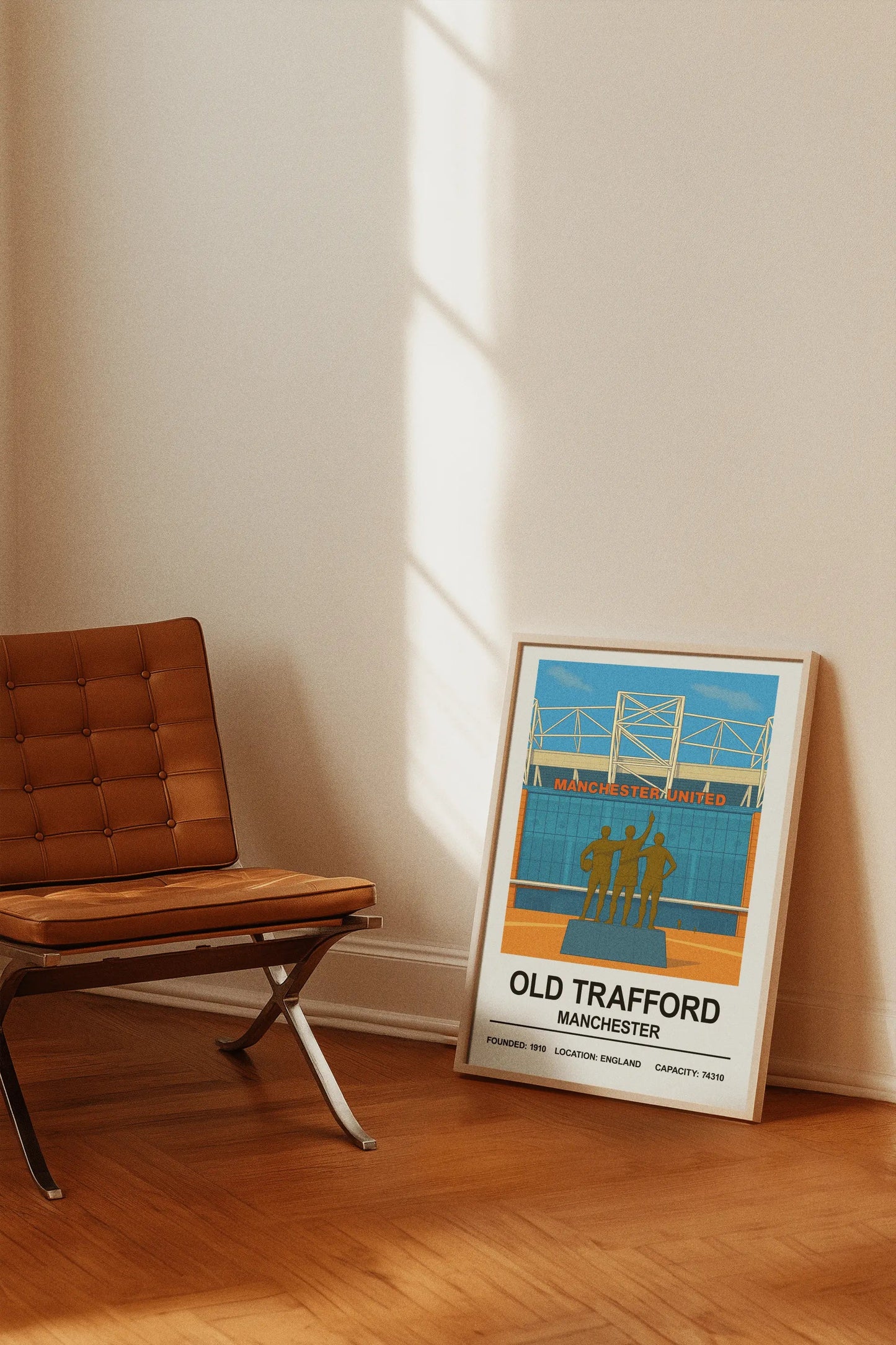 Framed poster of Old Trafford in Manchester leaning against a wall next to a wooden chair.
