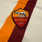 Close-up of the 2014 Roma logo with 'Roma' and '1927' on a striped background