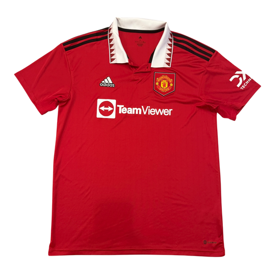 Red sports jersey with white TeamViewer branding on a white background. The jersey has a white collar and three black shoulder stripes. There is a white DCX technology on one sleeve. This is the Manchester United 2022-2023 Home Shirt