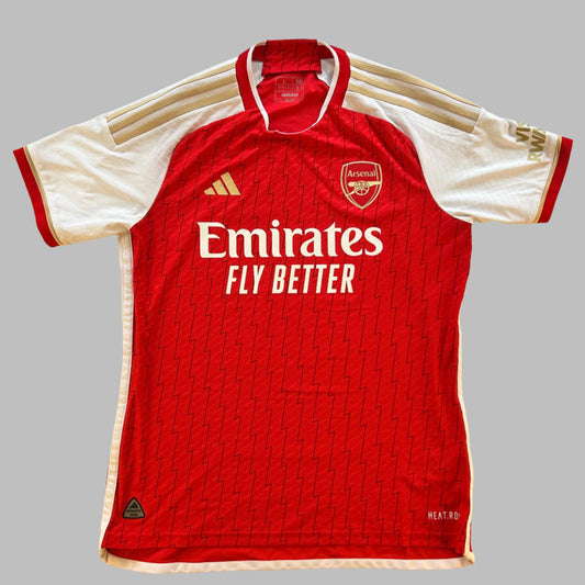 Arsenal 2023/2024 Authentic Home Shirt front. A zigzap pattern on a red shrit. The sleeves are white with gold 3 stripes and Adidas logo