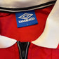 Close-up of a red jacket with a white collar and black zipper, featuring an Umbro label.