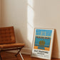 Framed poster of Old Trafford in Manchester leaning against a wall next to a wooden chair.